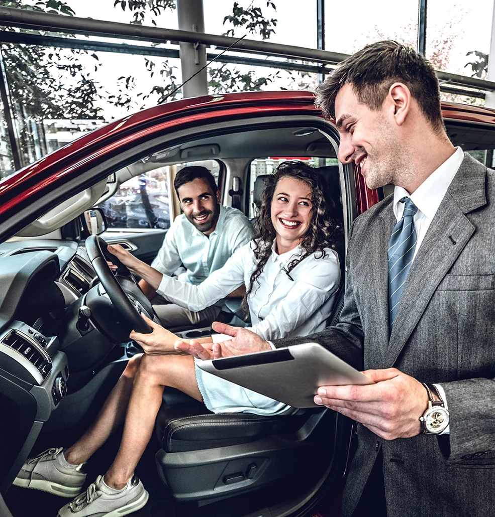 A man and woman in a car, engaged in conversation while driving on a sunny day.