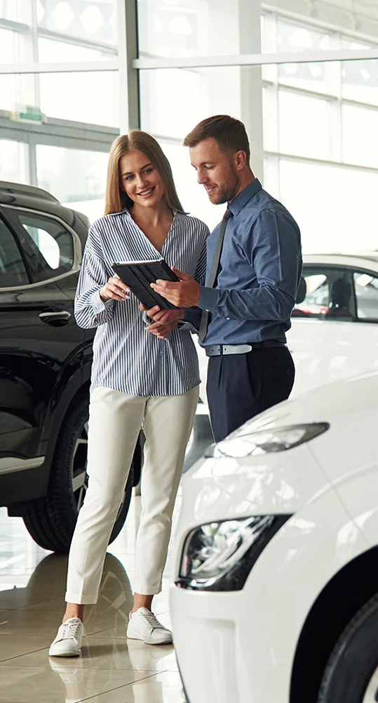 A couple stands in a car showroom, attentively inspecting a vehicle while engaged in conversation.