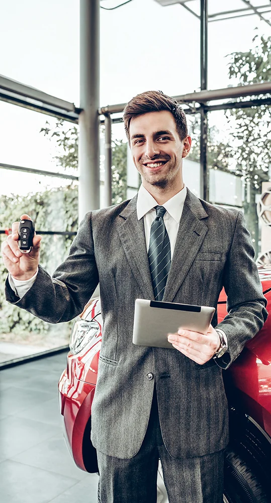 A professionally dressed man holds a tablet and a car key, showcasing a blend of technology and automotive readiness.