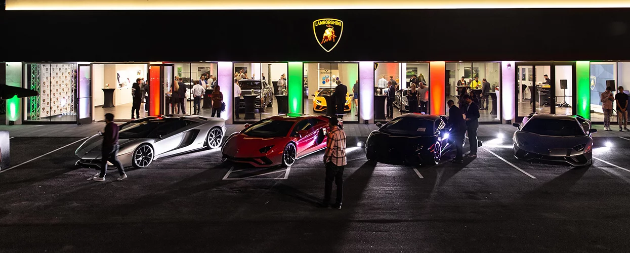 Guests attending a Lamborghini dealership event with luxury supercars displayed outside the showroom at night