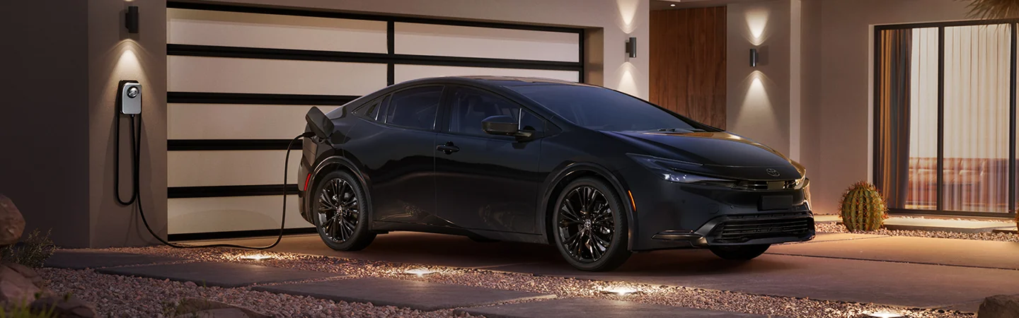 Front side view of a black 2026 Toyota Prius parked in a driveway charging