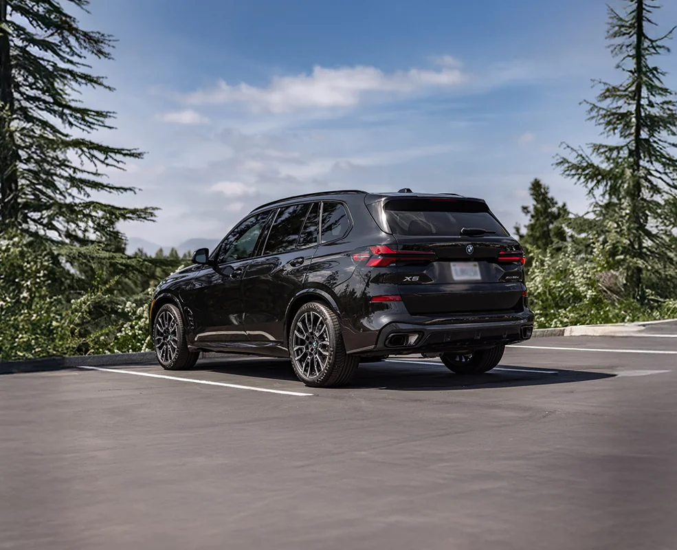 Back view of a parked black 2026 BMW X5 by the woods