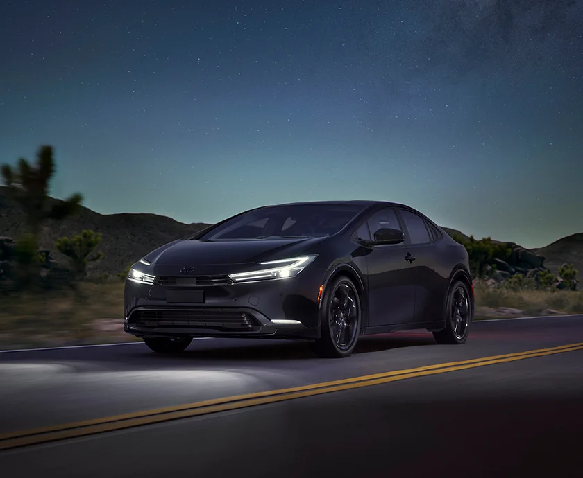 a front view of a black 2026 Toyota Prius with lights on