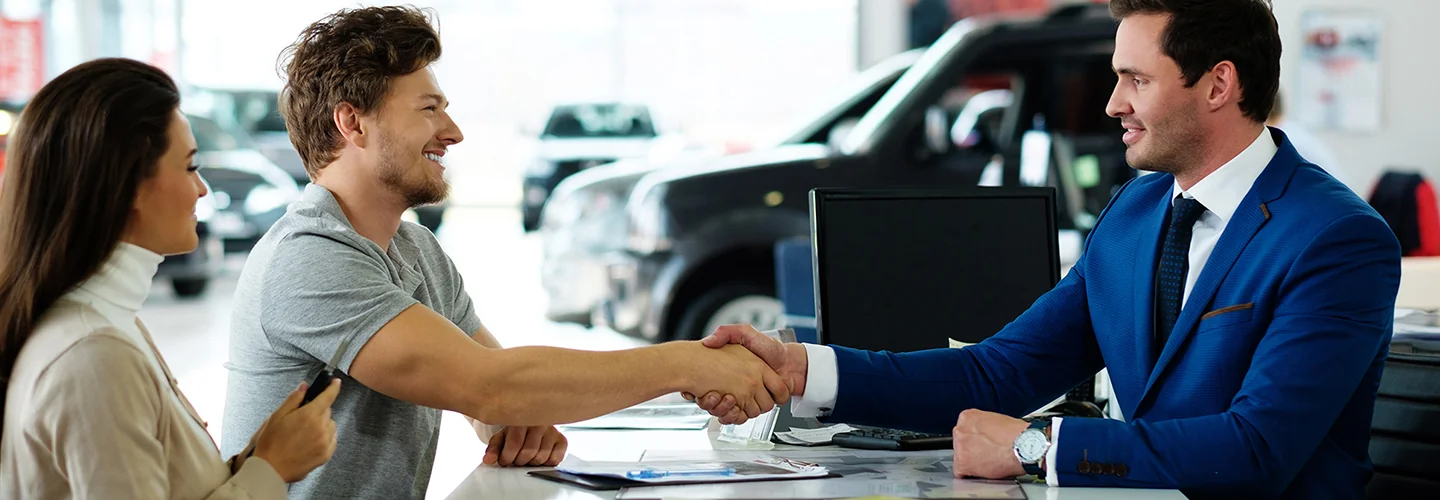 A man and woman shaking hands inside a car dealership, symbolizing a successful negotiation or agreement.