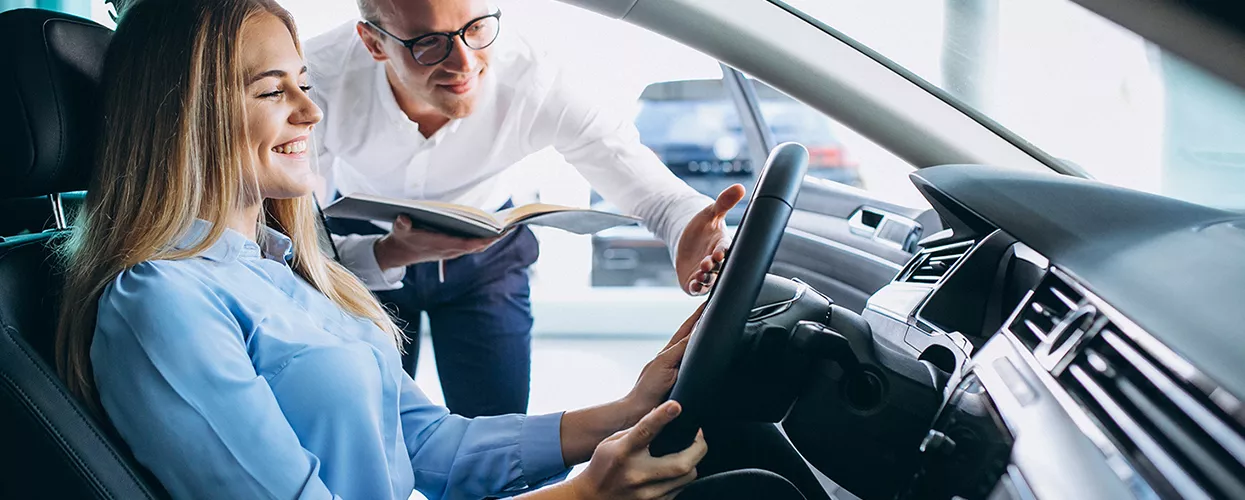 car salesman showing a woman the interior of a new vehicle