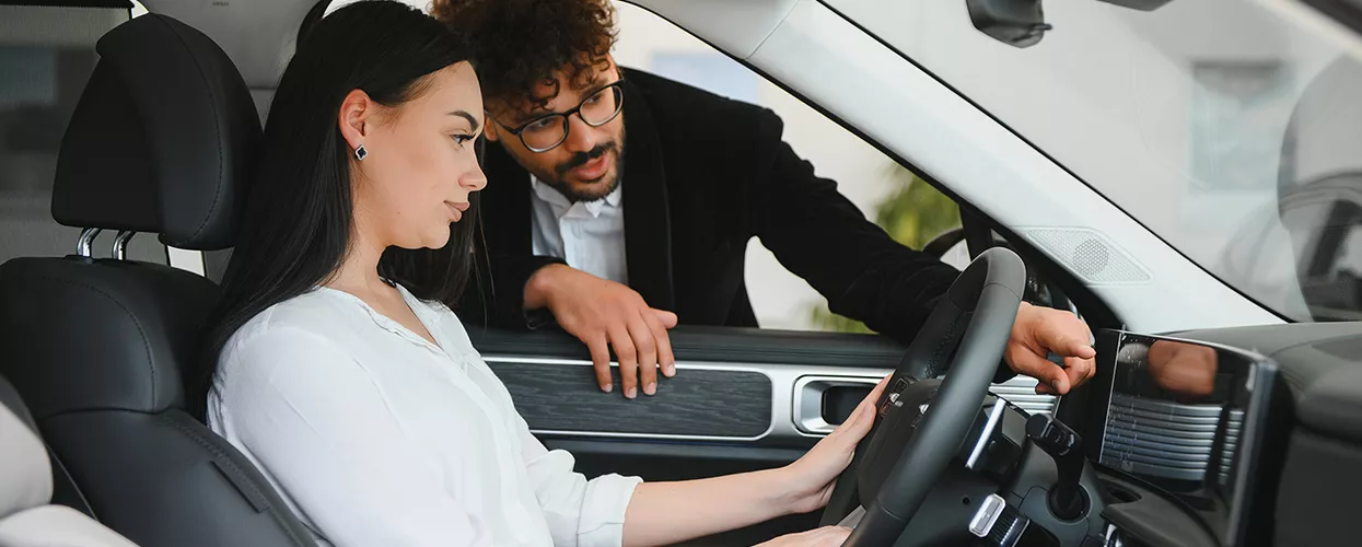 two peopl e standing by car and one sitting in car discussing features of the car