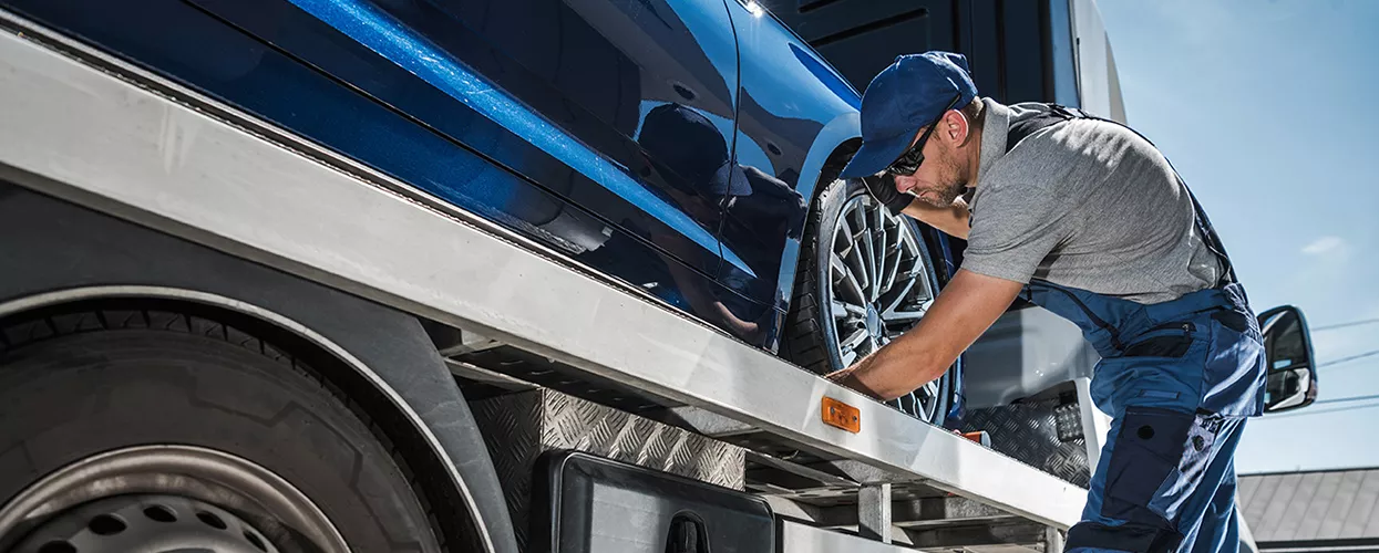 Service mechanic strapping a car to a trailer