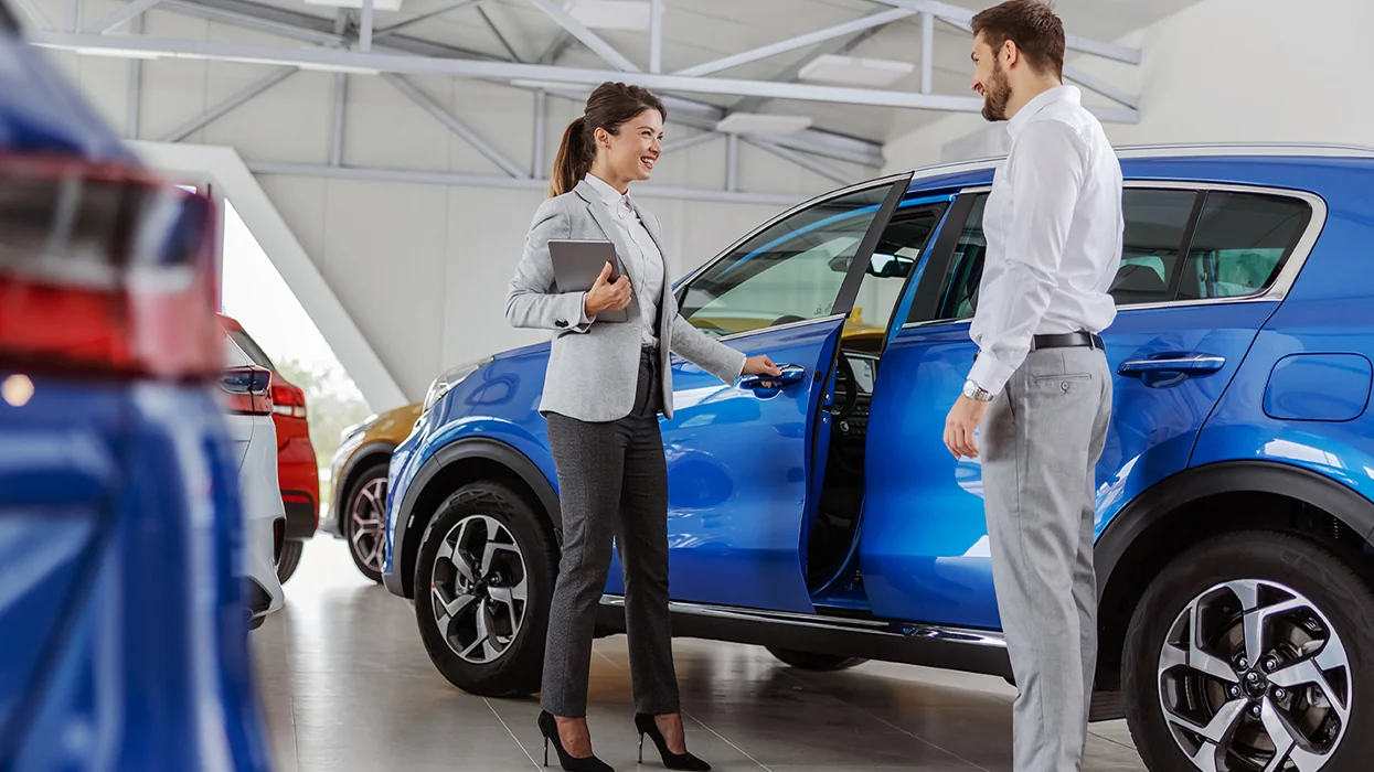 Sales person showing customer a used car in a showroom