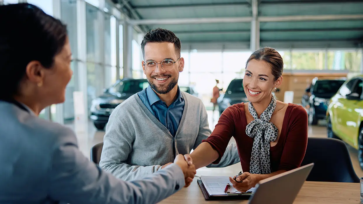 Service mechanic showing a customer a clipboard with a car's hood open in the background