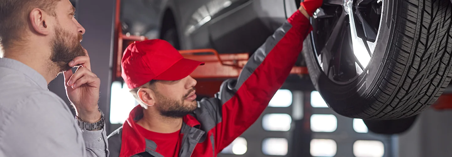 auto mechanic showing another person car wheel on a lift