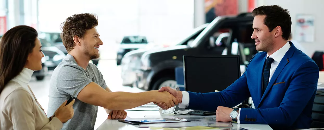 Couple shaking hands with a car salesman