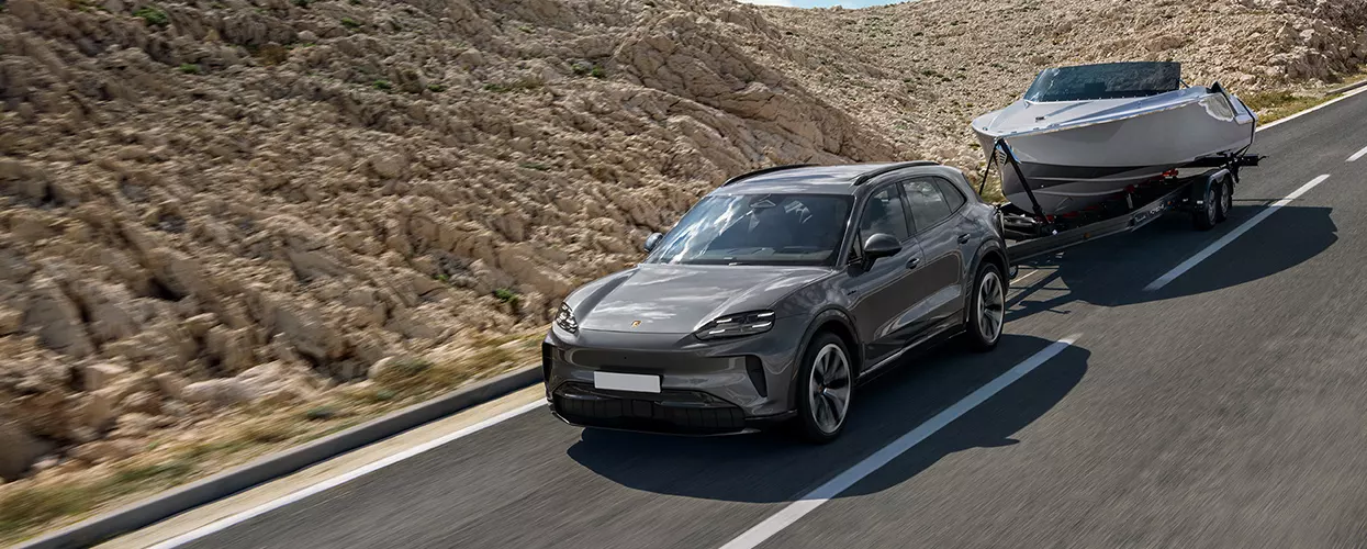 2026 Porsche Cayenne luxury SUV driving on a road towing a small boat