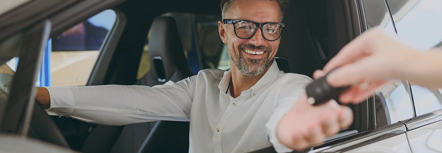 person smiling in a car being handed keys