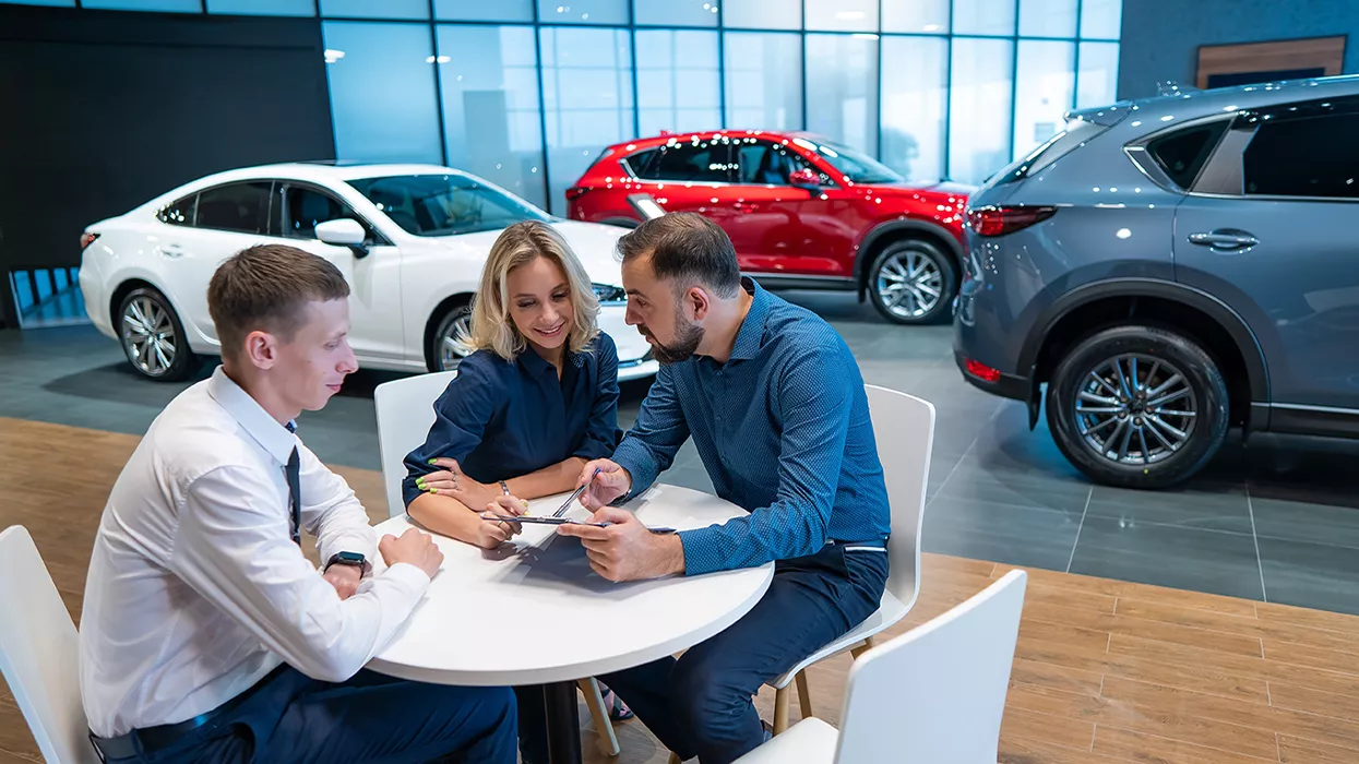 Three people sitting around a table at a car dealership