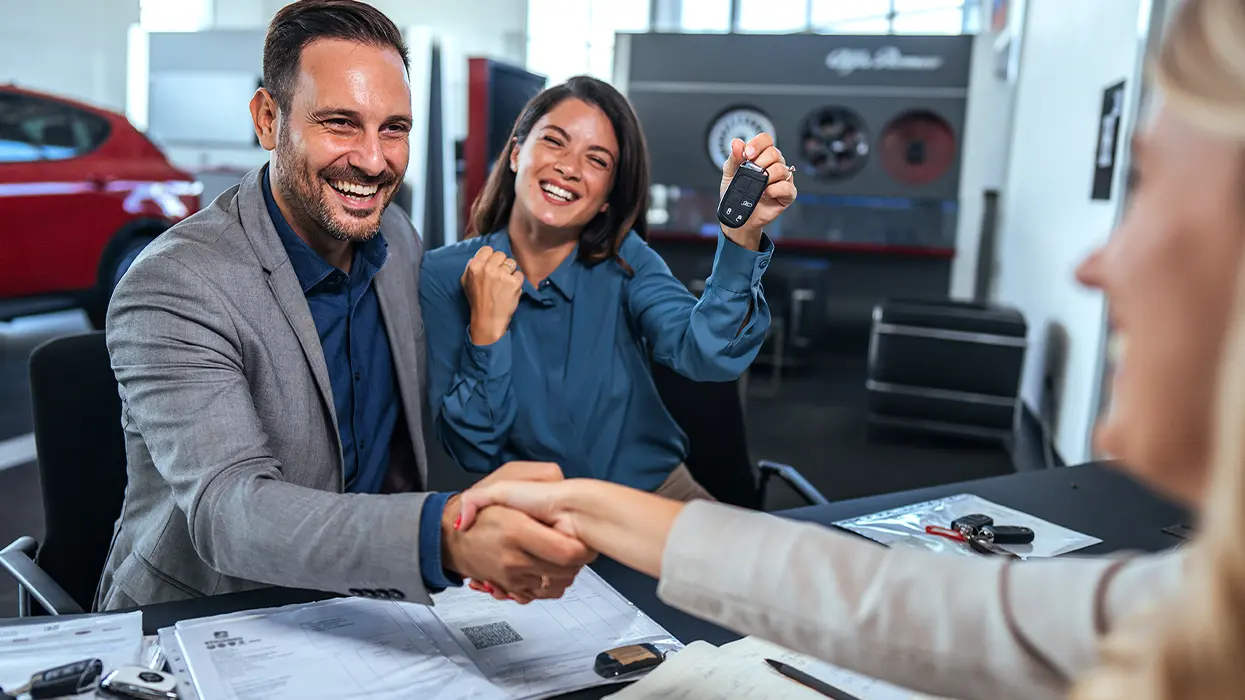 Service mechanic showing a customer a clipboard with a car's hood open in the background