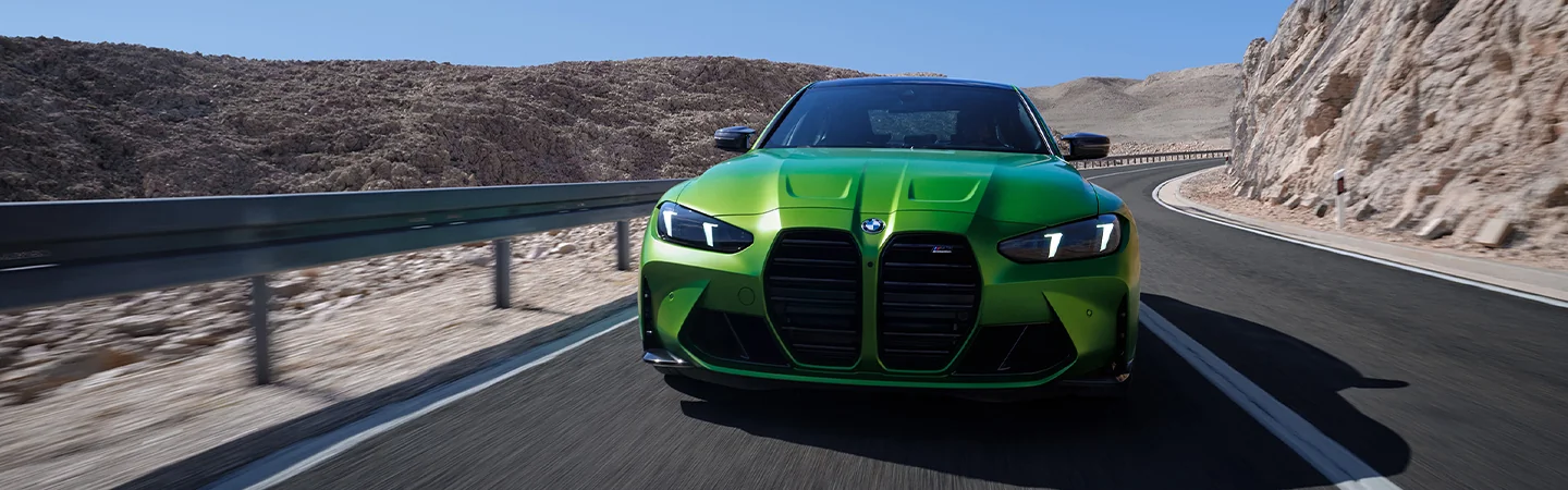 A green 2025 BMW 330i driving on a road next to some hills