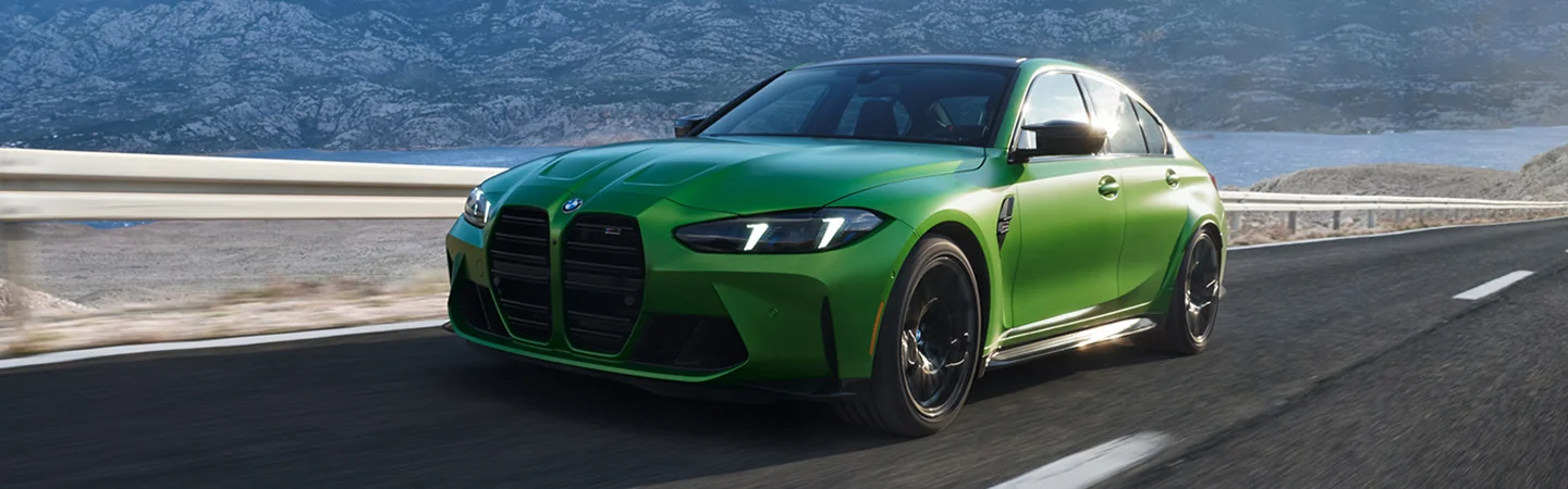 A green 2025 BMW 330i driving next to a lake