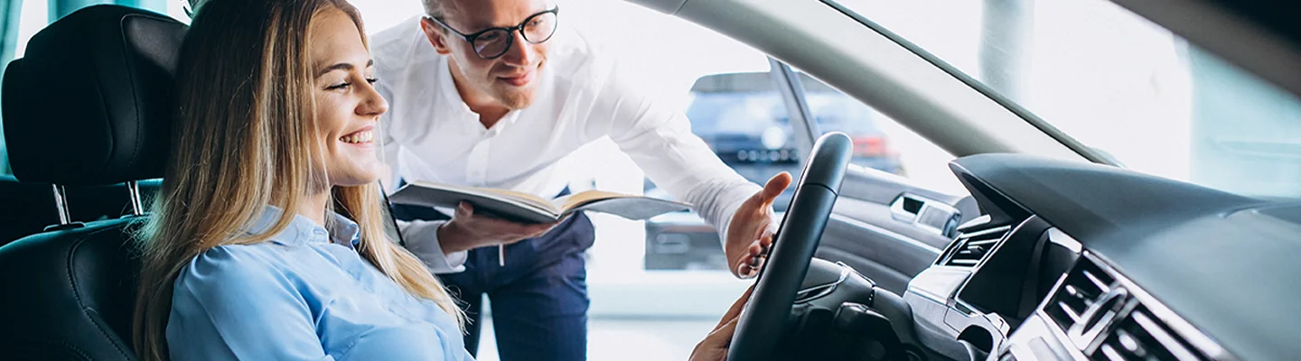 person smiling in drivers seat with another person speaking out side door