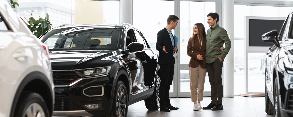 A couple stands outside a car dealership, discussing their options while looking at the cars available.