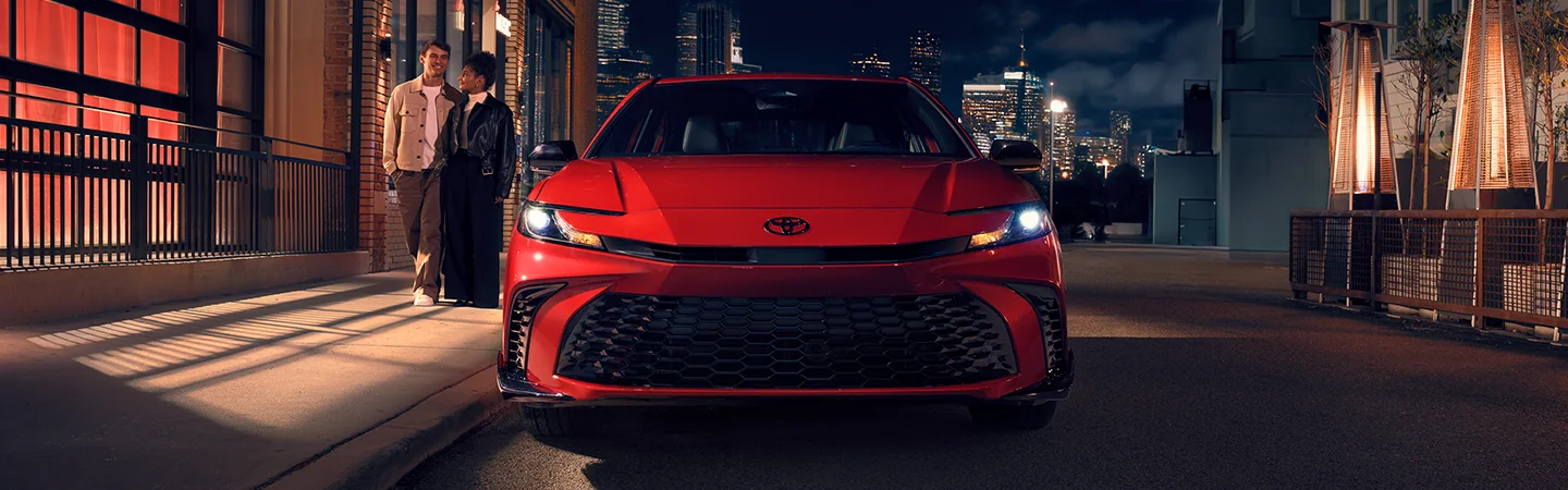 Front view of a parked red 2026 Toyota Camry with a city in th ebackground