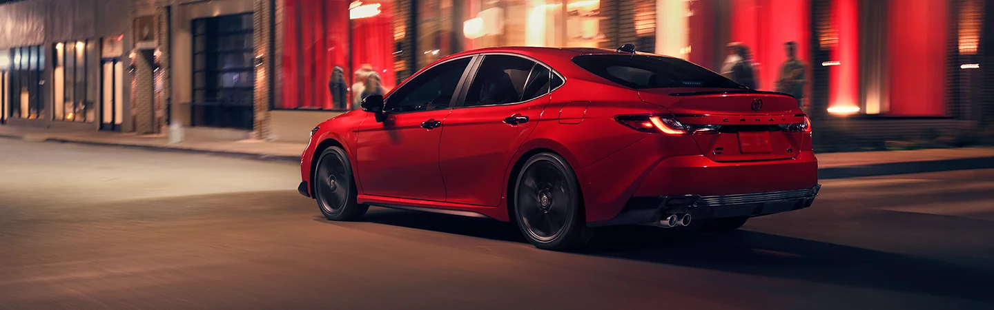 Back side view of a red 2026 Toyota Camry driving in the city