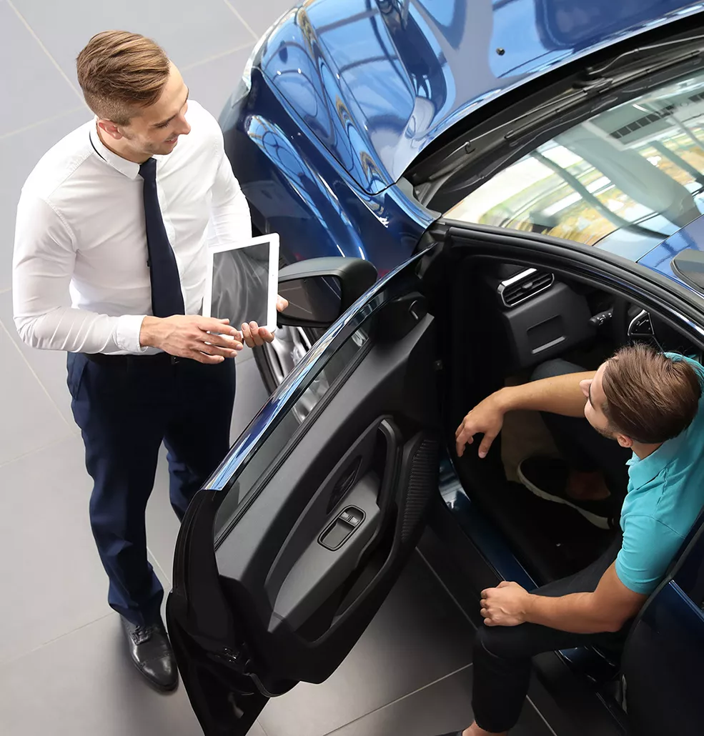 Customer sitting inside a new vehicle with a car salesman standing outside