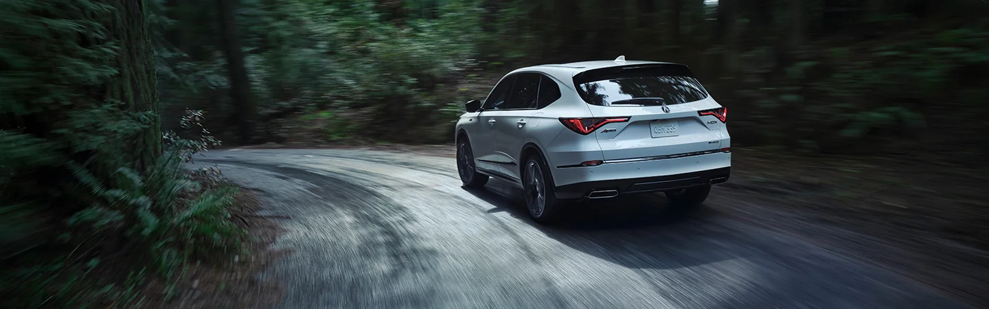 Back view of A white 2025 Acura MDX driving in the woods