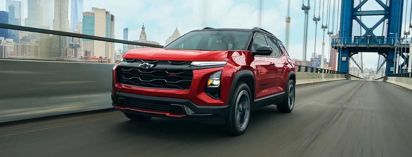 a red 2026 Chevrolet Equinox LT driving over a city bridge