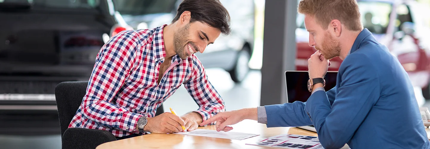 one person signing some papers as the car dealership salesperson looks on