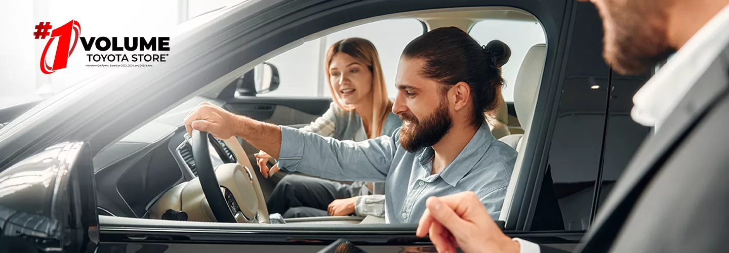 man and woman sitting inside of a car with the salesman talking to them through the window