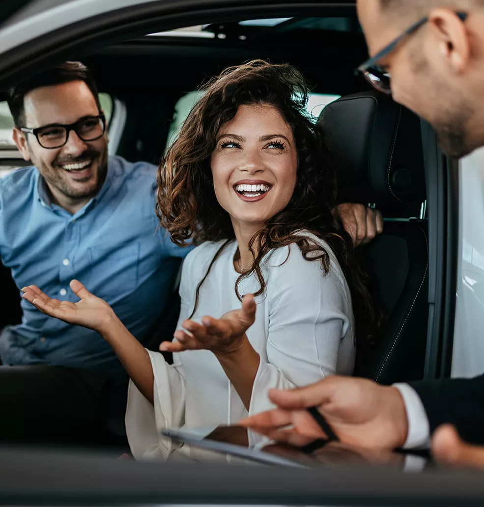 Car salesman talking to a couple sitting in a new car