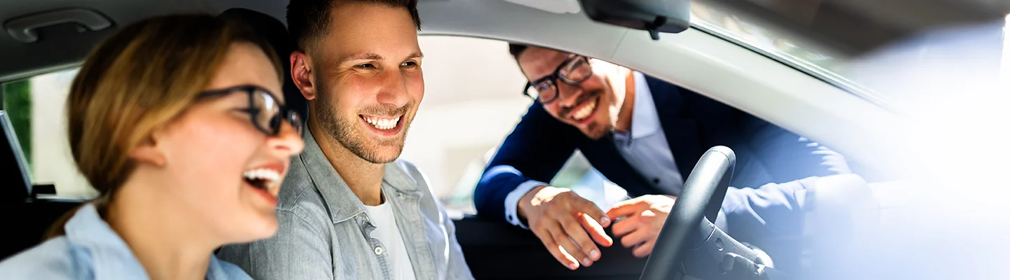 two people in car with another outside car smiling looking over new car