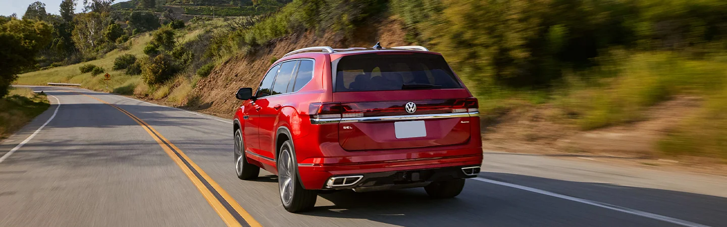 Rear view of the 2026 Volkswagen Atlas driving down a country road with hills in the background