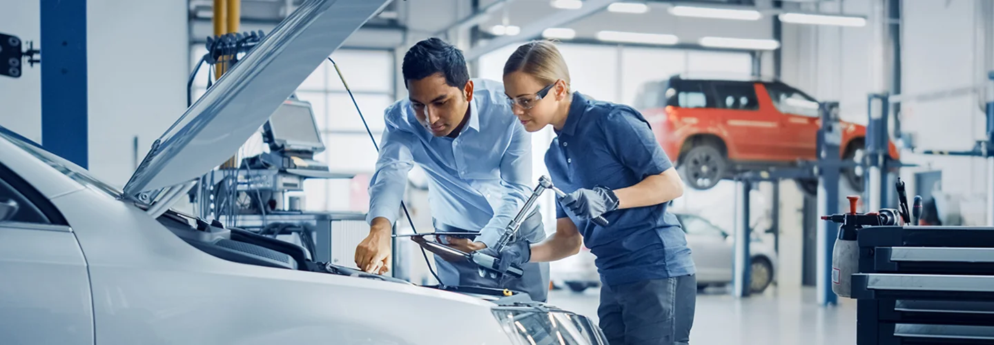 In a garage, two men are collaborating on car repairs, focused on the vehicle with various tools nearby.