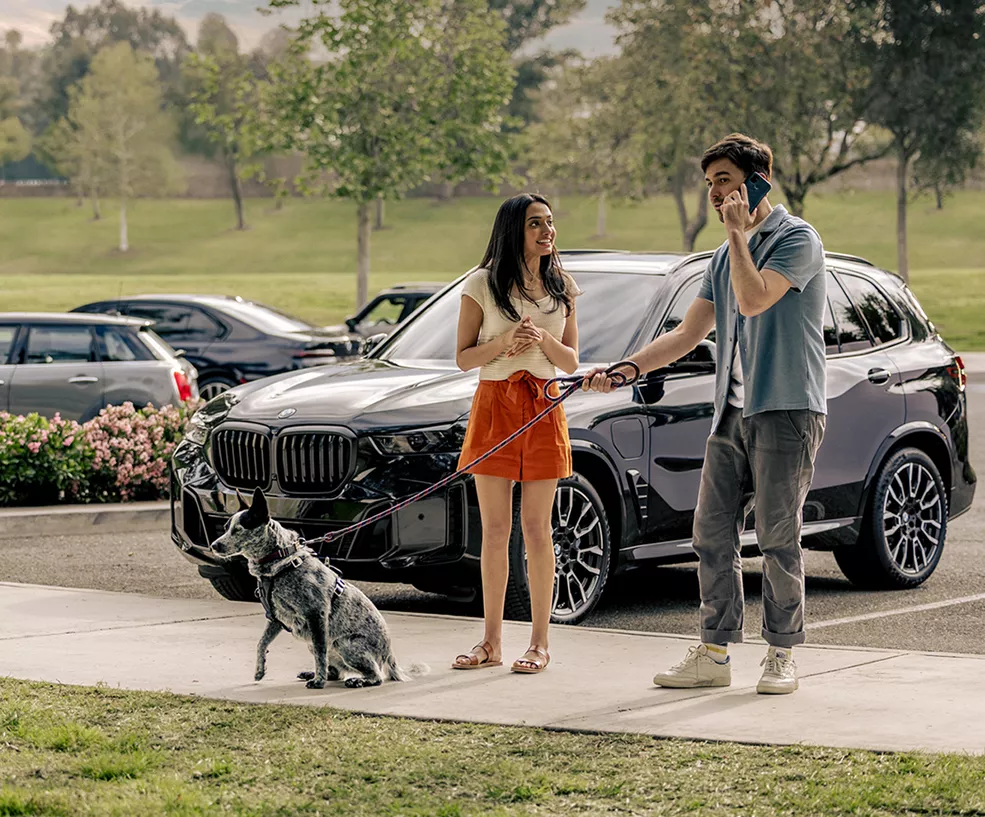 Couple walking thier dog and standing in frotn of a 2026 BMW X5