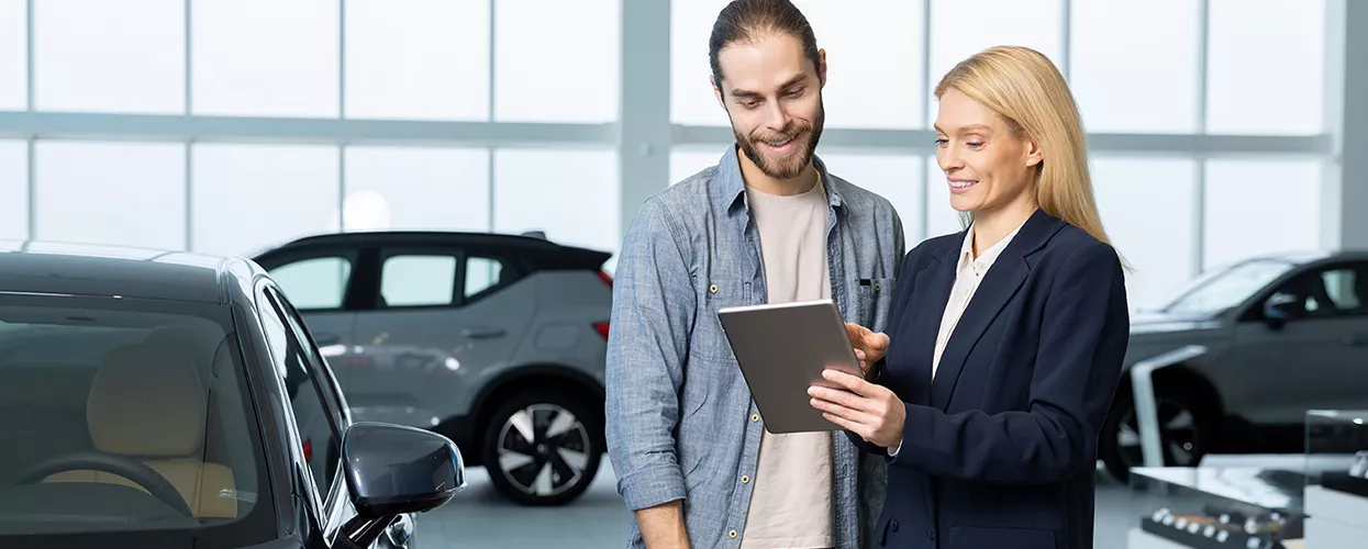 Car saleswoman showing someone a tablet in a car dealership