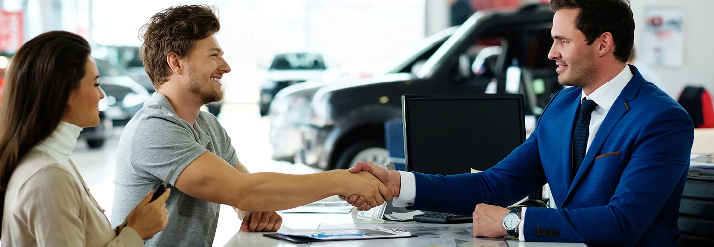 Customers shaking hands with a sales person as they make a deal on a new car