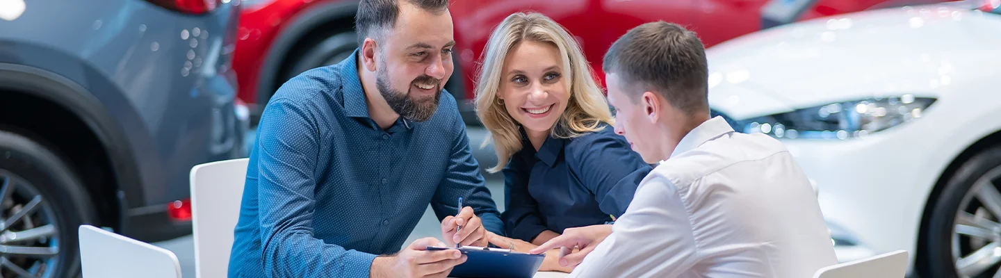 couple sitting at salesperson desk with salesperson discussing a car loan