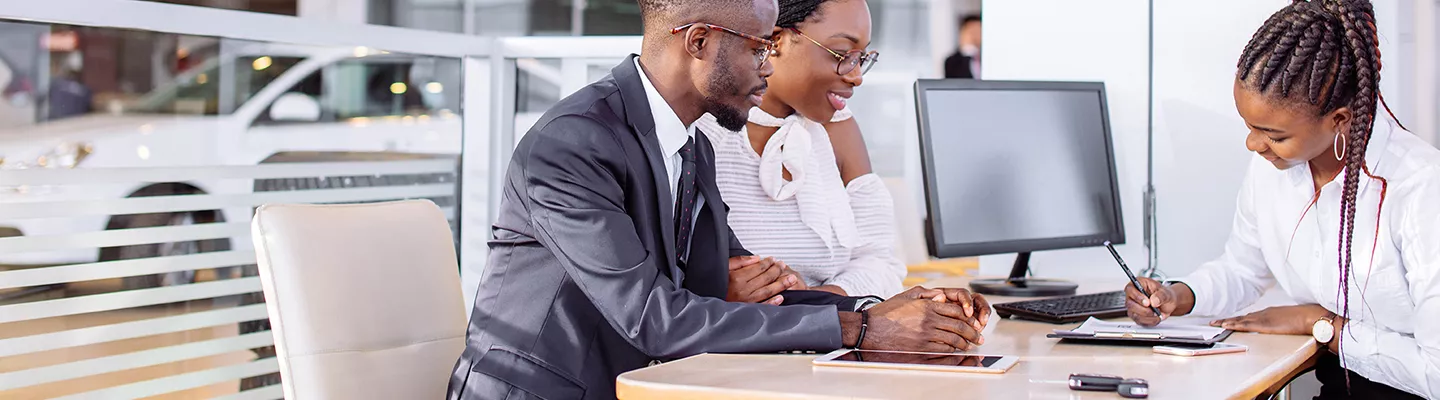 Customers sit with salesperson in an office at a dealership