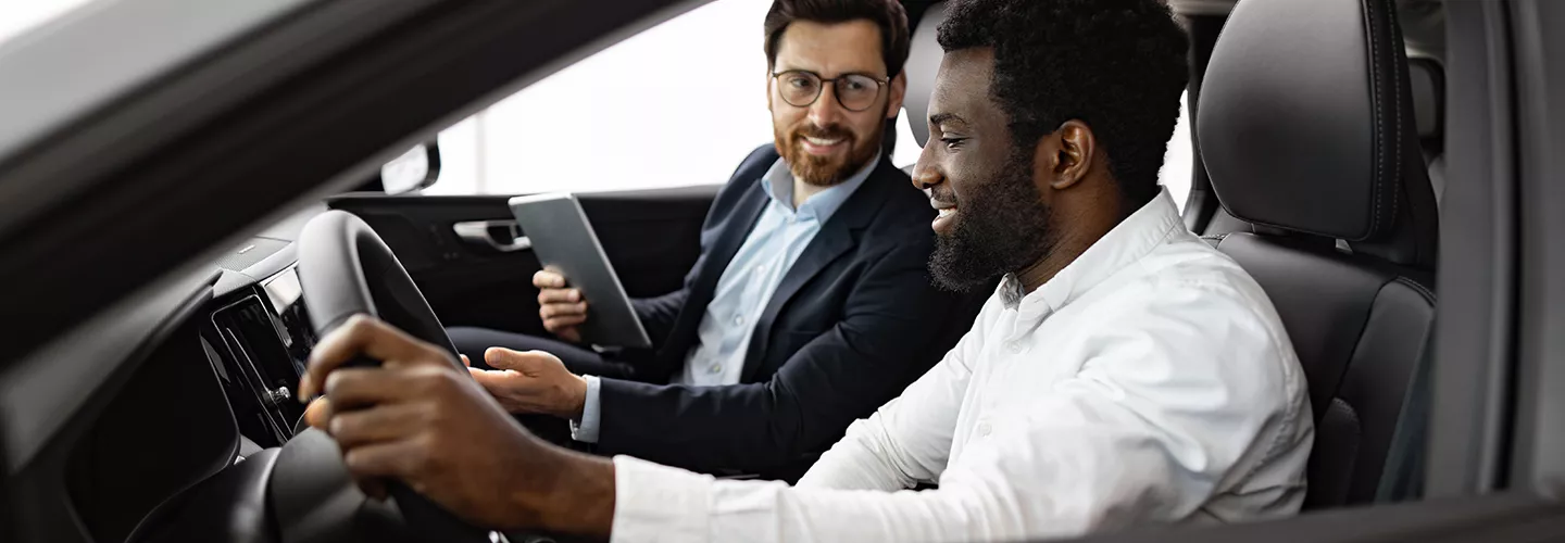 Man sitting in car with a car salesman smiling