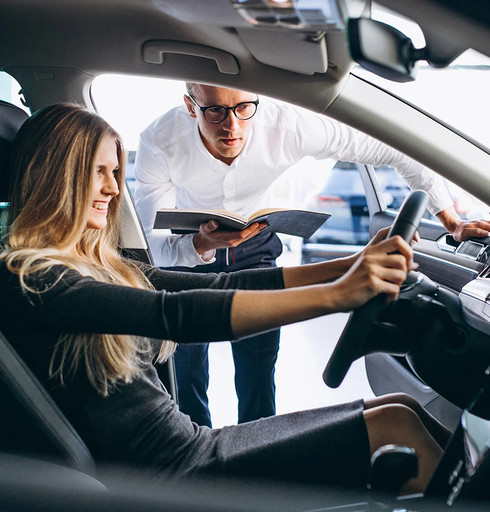 Sales persont alking to a customer while they check out the inside of a new car