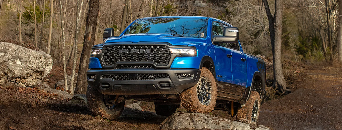 a bright blue 2026 RAM 1500 Tradesman showing some offroad moves up a hill in a forest