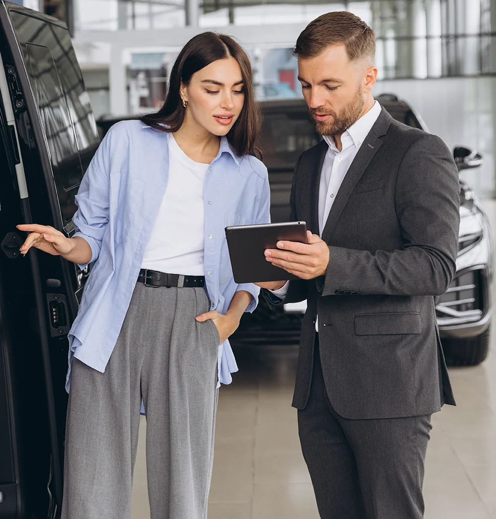 A man and woman examine a tablet while discussing options at a car dealership.
