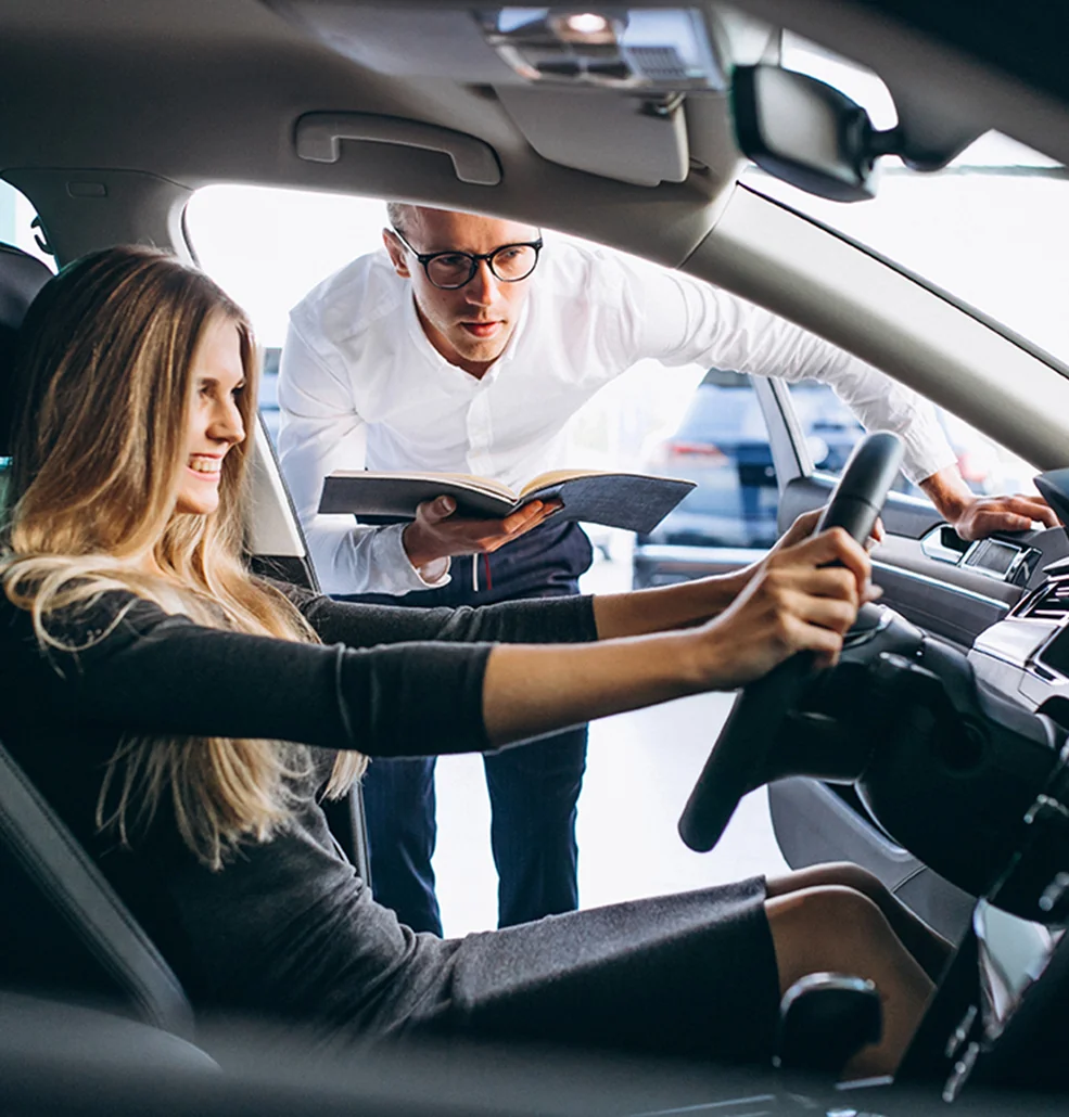 A man and woman are seated in a car, observing another car parked in front of them.