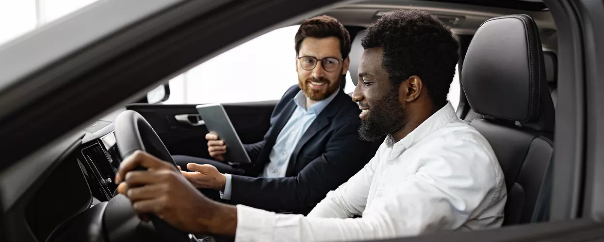 Car salesman talking to a customer sitting in a new vehicle at a car dealership