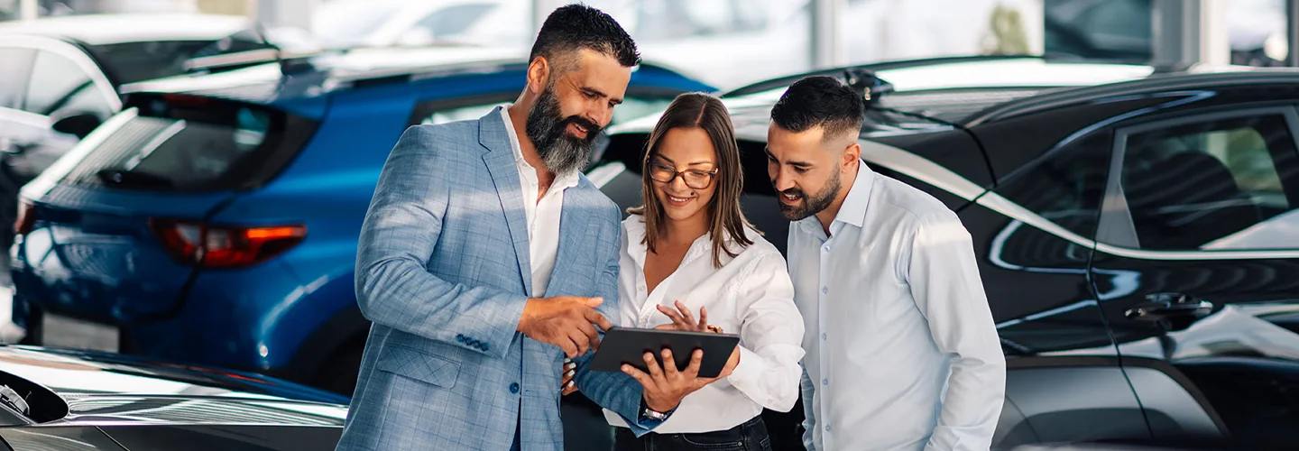 two people looking over details of a car purchase with salesperson in dealership