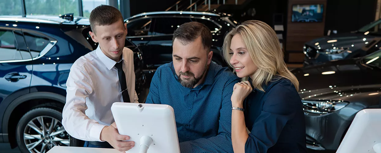 Three people looking at a tablet in a car dealership