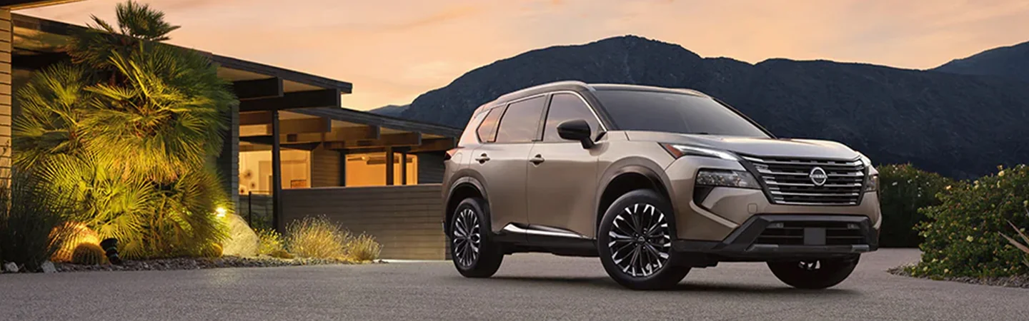 Side view of a parked tan 2024 Nissan Rogue in front of a house