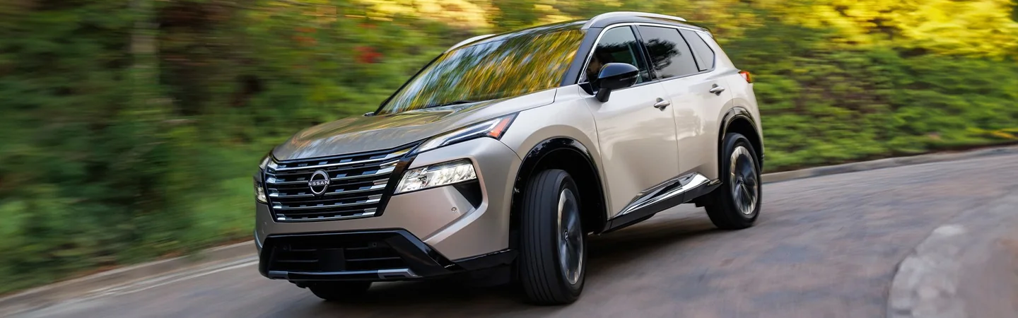 A tan 2024 Nissan Rogue driving on a road
