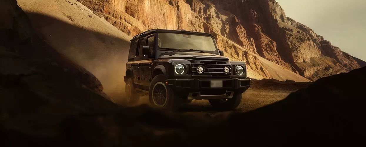 a view of a 2026 INEOS Grenadier Trialmaster offroad in desert by cliff